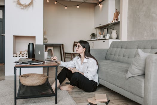 Asian woman working on laptop from cozy living room, showcasing modern home office setup.