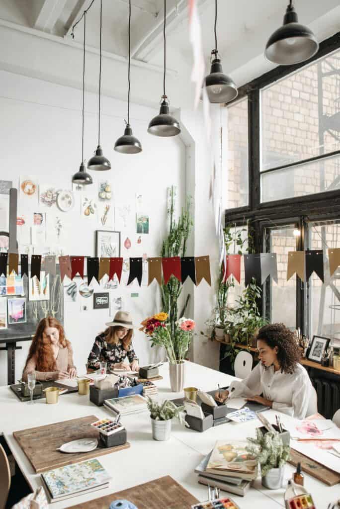Women engaged in artistic activities at a lively indoor workshop filled with decorations and natural light.