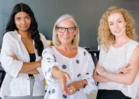 Three diverse businesswomen standing confidently in an office, showcasing teamwork and professionalism.