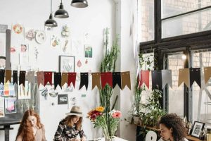 Women engaged in artistic activities at a lively indoor workshop filled with decorations and natural light.